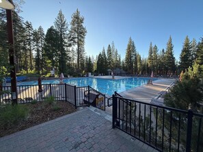 A swimming pool with a wooden deck and metal railings, surrounded by tall trees.
