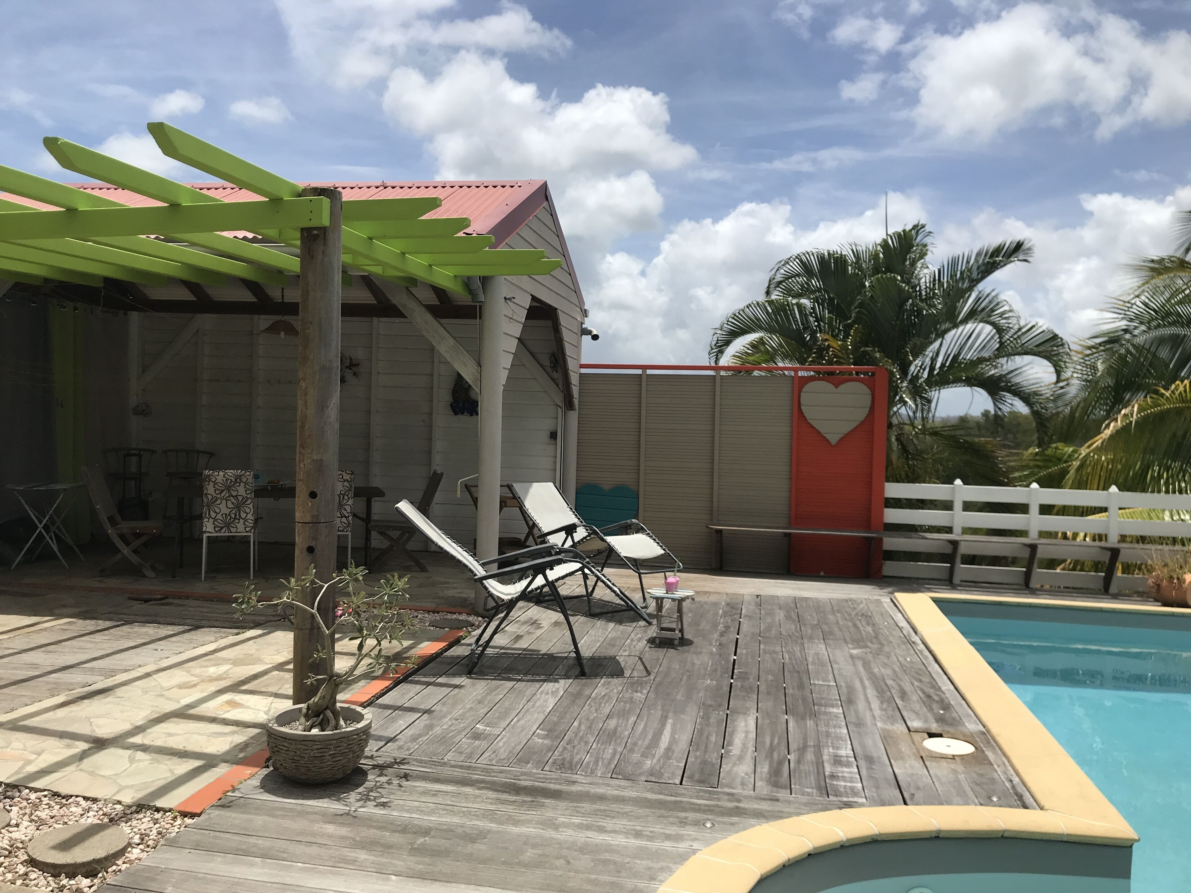 Eine Holzterrasse mit Liegestühlen, einem kleinen Pool und einem Gebäude mit rotem Dach.
