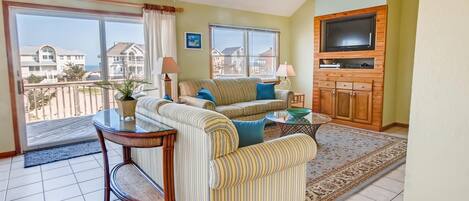 A living room with a sofa, a coffee table, a TV, and a view of the ocean.