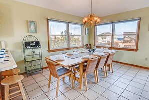 Un coin repas avec une grande table dressée pour six personnes, entourée de chaises en osier, et un lustre au-dessus.