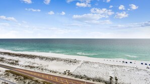 A beach with a road running parallel to the shore, a clear sky, and the ocean.