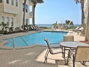 A pool area with lounge chairs and a table, overlooking the ocean.