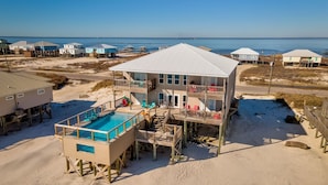 A beachfront house with a pool, multiple balconies, and a view of the ocean.