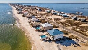 An aerial view of a coastal area with beach houses, a swimming pool, and a pier extending into the water.