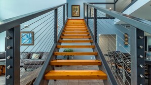 A staircase with wooden steps and metal railings, leading to a landing area with a sofa and a plant.
