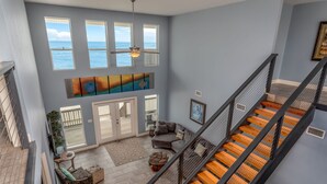 A spacious living area with a view of the ocean, a staircase with wooden steps, and a ceiling fan.
