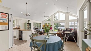 A spacious kitchen with white cabinetry, a dining area with a blue tablecloth, and large windows offering views of the outdoors. - Vast Open Floor Home with Fire Pit on the Lake (Pullman)