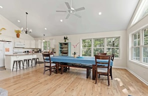 A spacious kitchen with white cabinets, a large island, and a dining area with a blue table and wooden chairs.