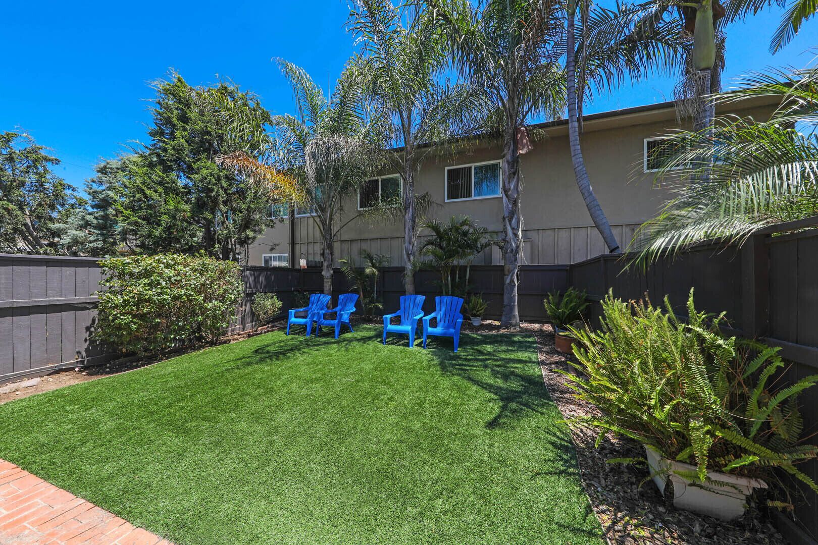 A backyard with artificial grass, a wooden fence, and several blue chairs.