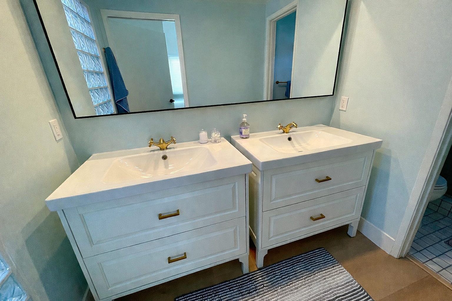 A bathroom with two white sinks, a large mirror, and a blue patterned rug.