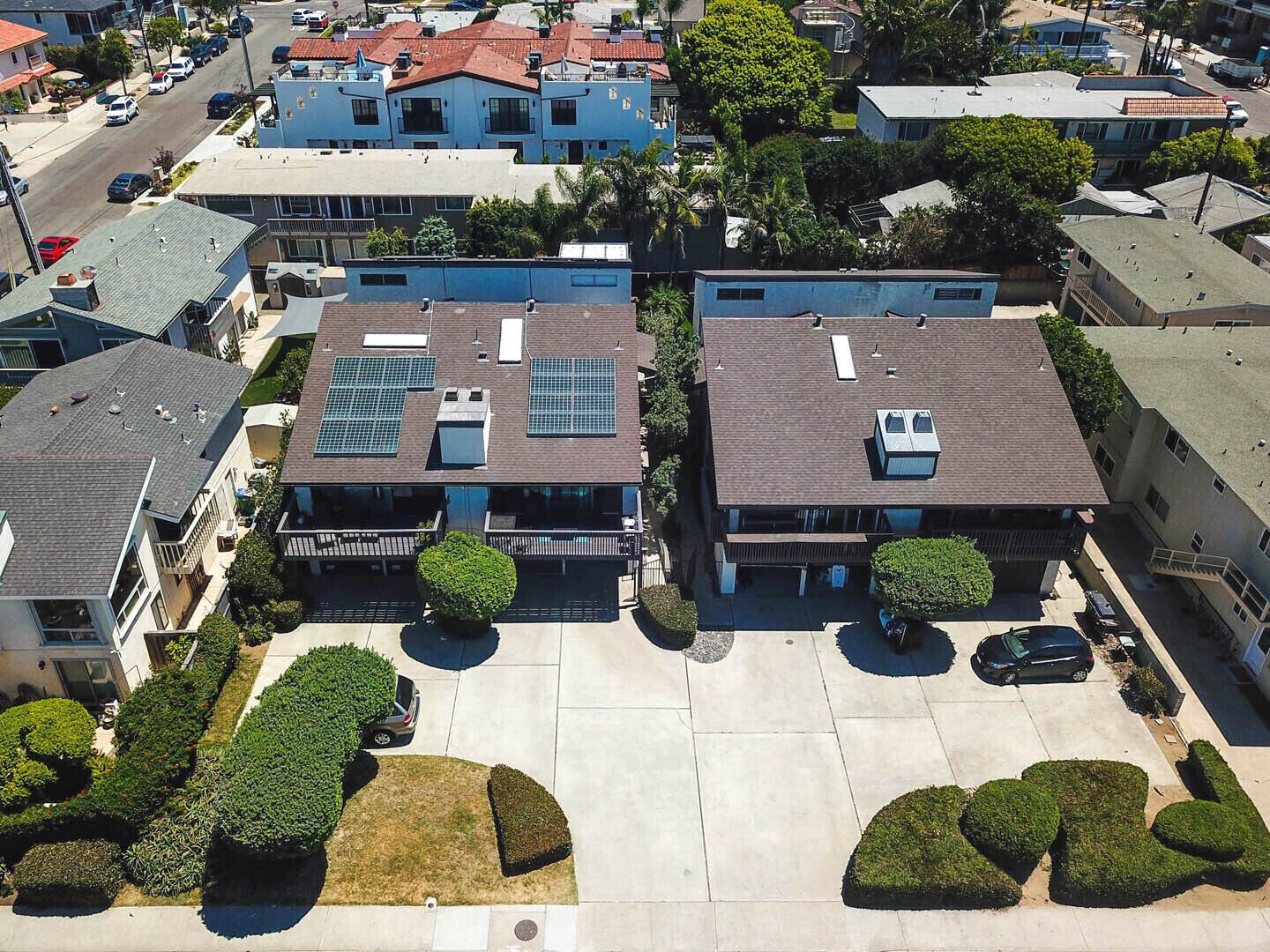 A residential area with two houses featuring solar panels, a parking lot, and well-maintained lawns.