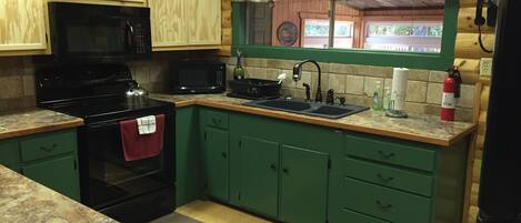 A kitchen with green cabinets, a black stove, a microwave, and a sign above the sink that reads 'Fishing Stories Told Here'.