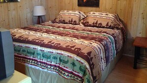 Ein Bett mit gemusterten Betttextilien, ein Bild eines Bootes an der Wand und eine Lampe neben dem Bett.