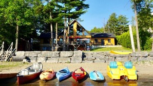 A lakeside property with a wooden cabin and a dock with colorful kayaks.