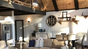 A spacious living room with a high ceiling, wooden beams, a large round mirror, and a cozy seating area with a sofa and armchairs.