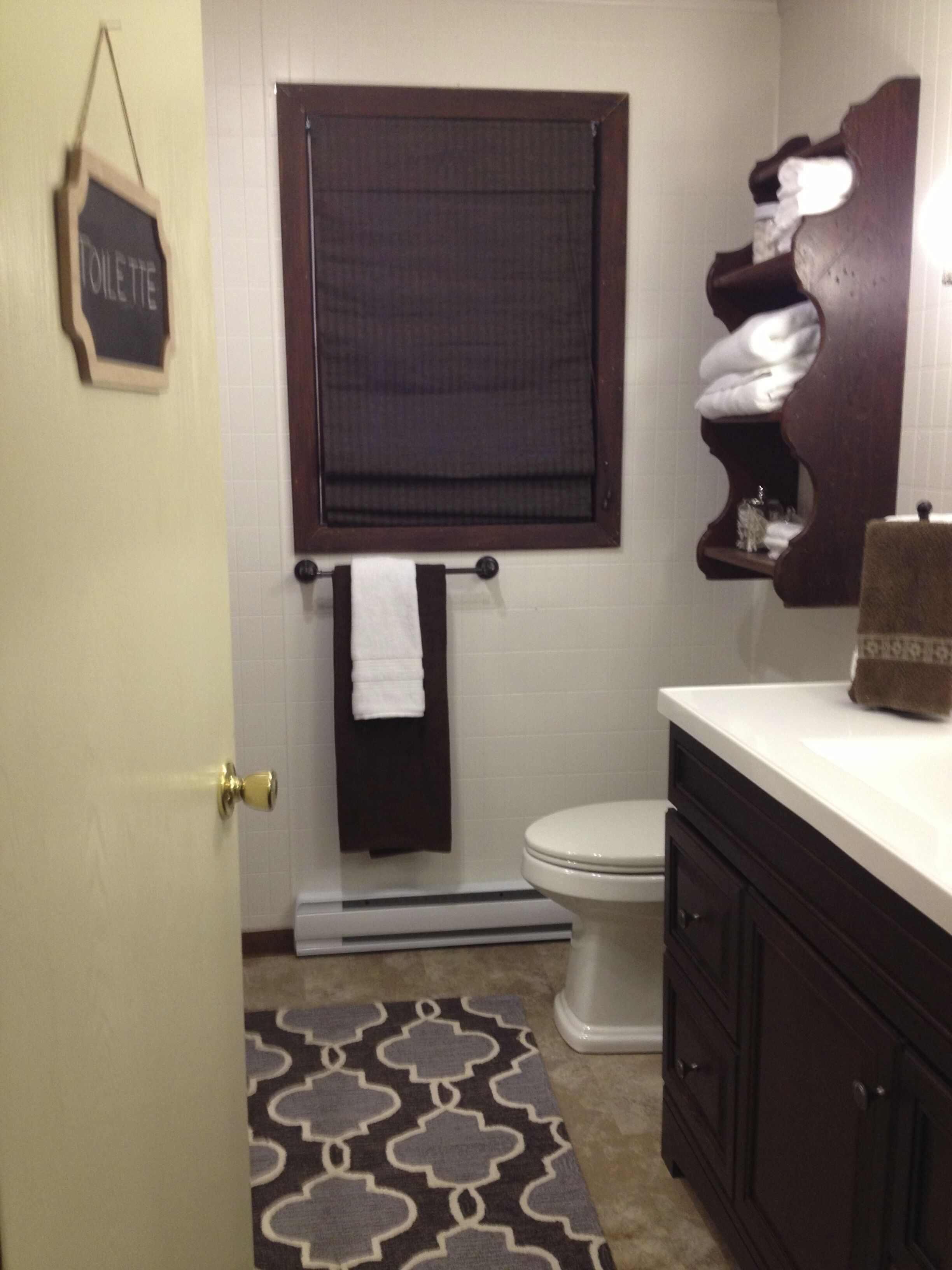 A bathroom with a toilet, a towel rack, a bath mat, and a wooden shelf with towels.