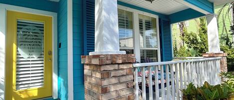 A house with a blue exterior, a yellow door, and a brick pillar.