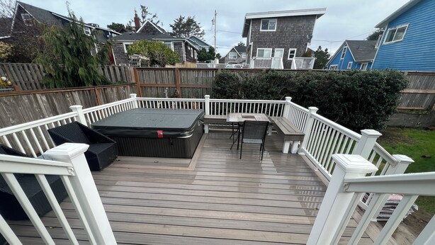 Um deck de madeira com hidromassagem, área de estar externa e vista para as casas vizinhas.