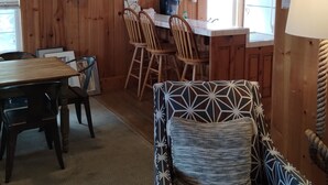 Um interior em madeira com uma mesa de jantar, cadeiras, uma poltrona estampada e um frigorífico.