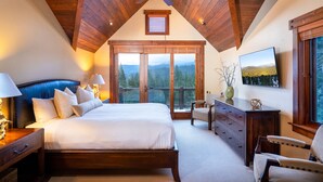 Un dormitorio con una cama grande, techo de madera y vistas a montañas a través de amplios ventanales.