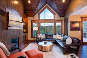 A spacious living room with a large sectional sofa, a fireplace, and large windows offering a view of the outdoors.