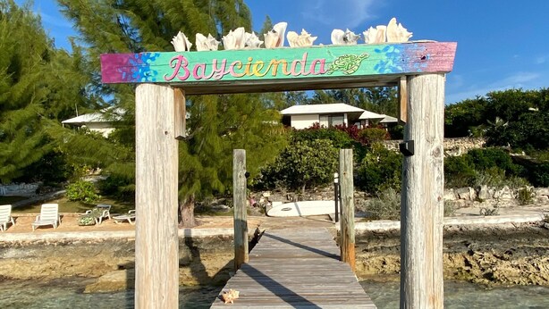 Eine Holzstege führt zu einem Strandabschnitt, auf dem ein Schild mit dem Schriftzug "Bayciennda" steht.