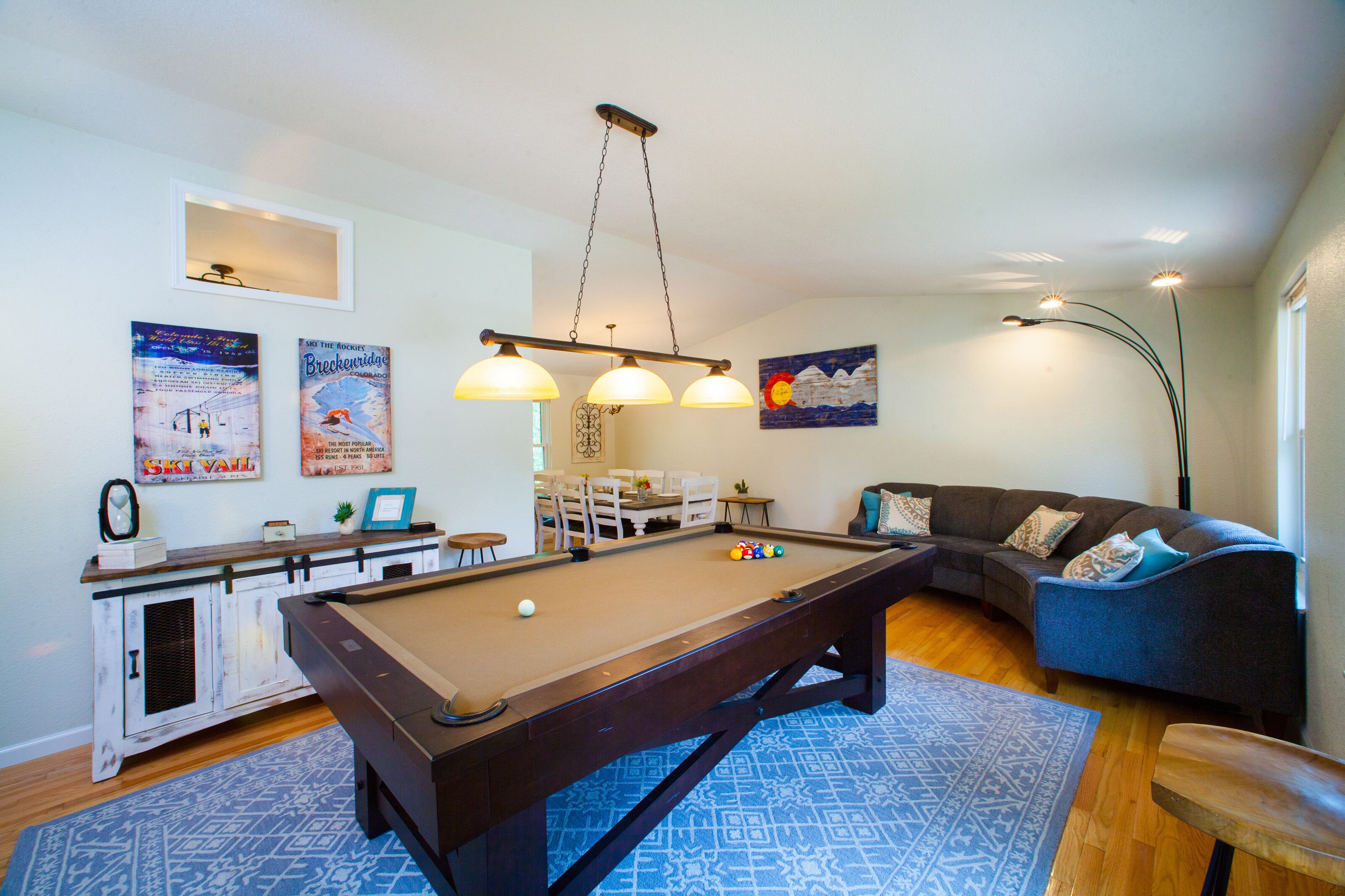 Une table de billard dans un salon, avec un tapis à motifs bleus, un canapé avec des coussins et un tableau accroché au mur.