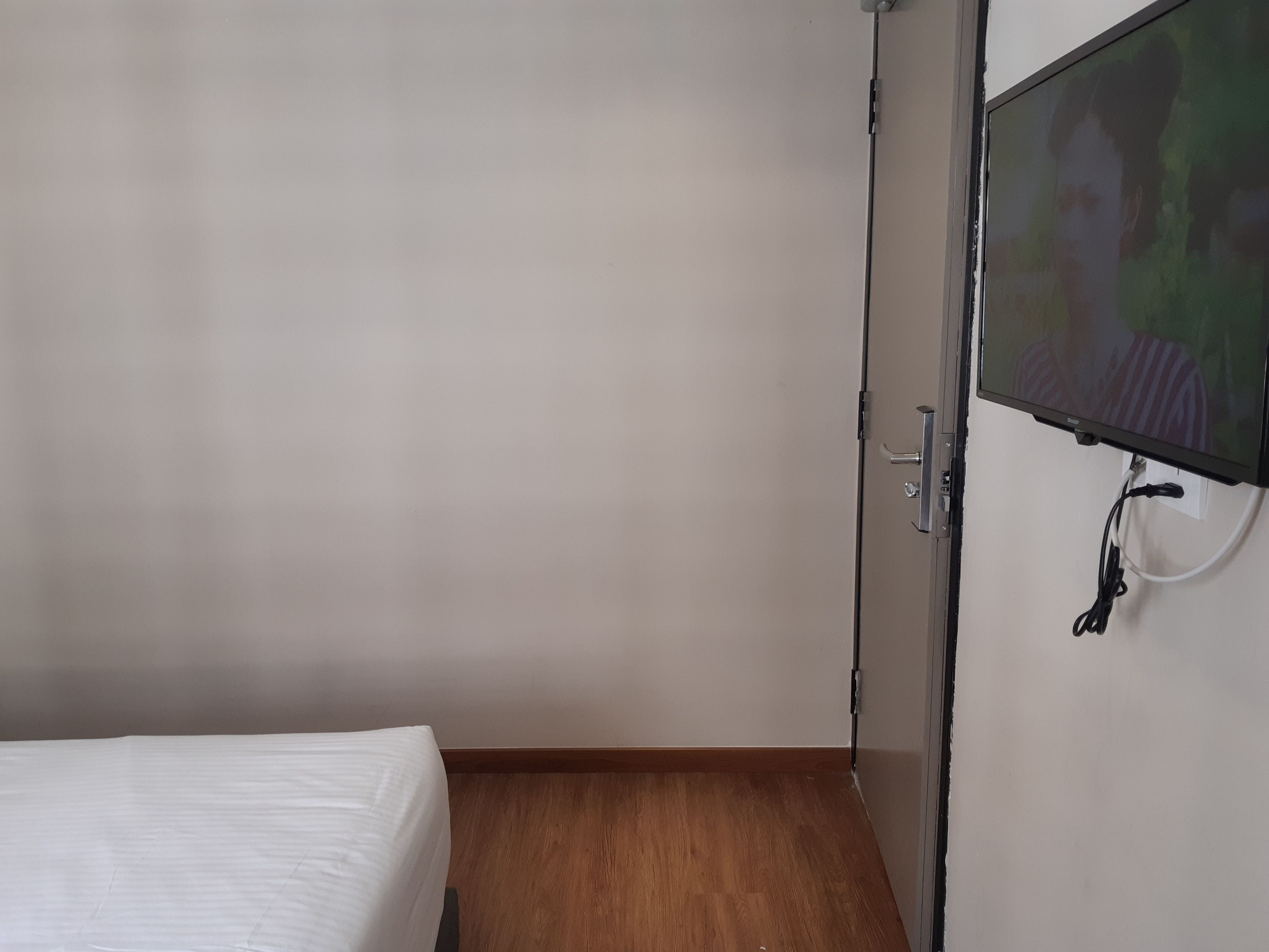 Una habitación con cama, televisión montada en la pared y piso de madera.
