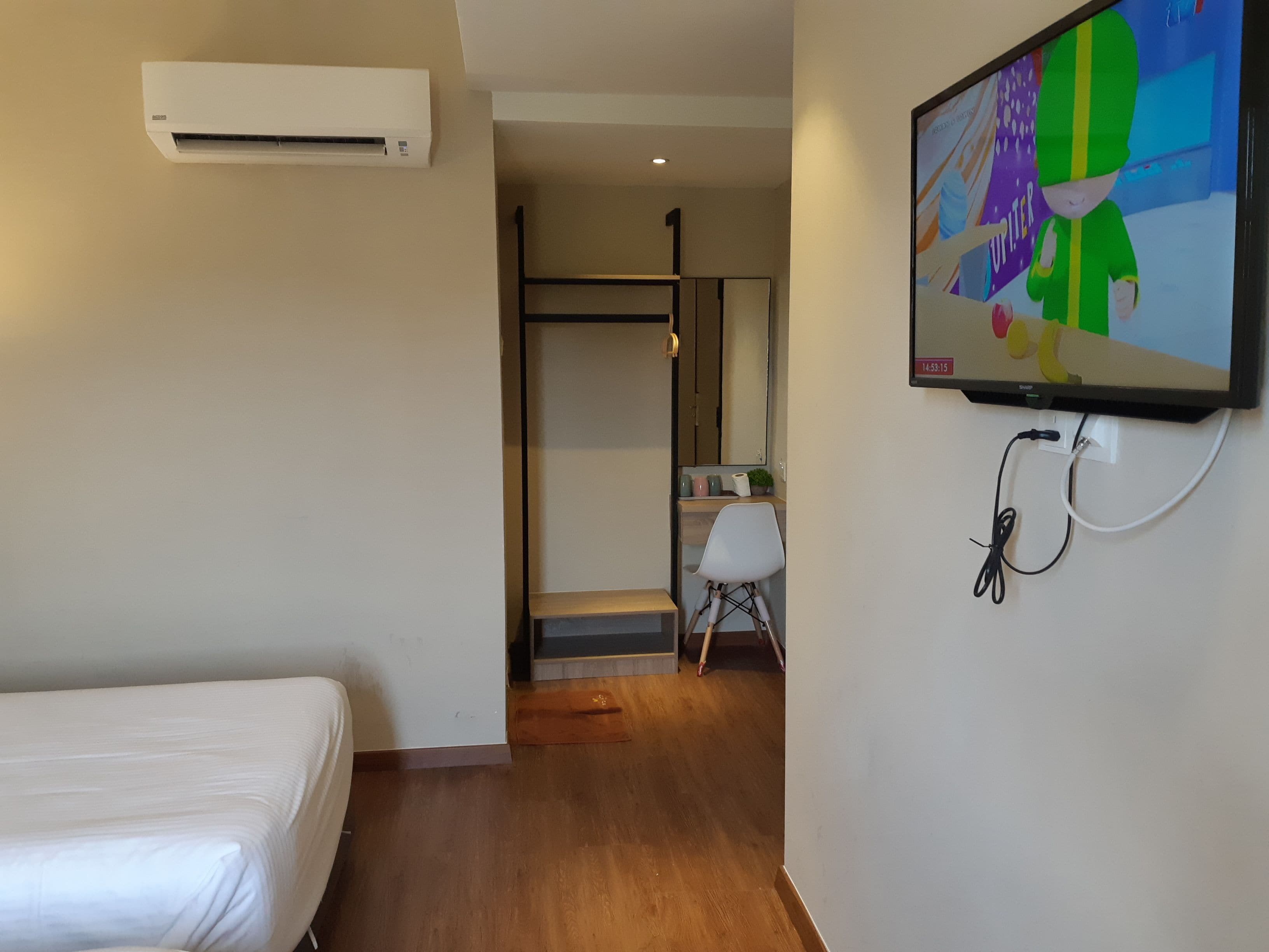 A hotel room with a bed, an air conditioning unit, a TV mounted on the wall, and a wooden floor.