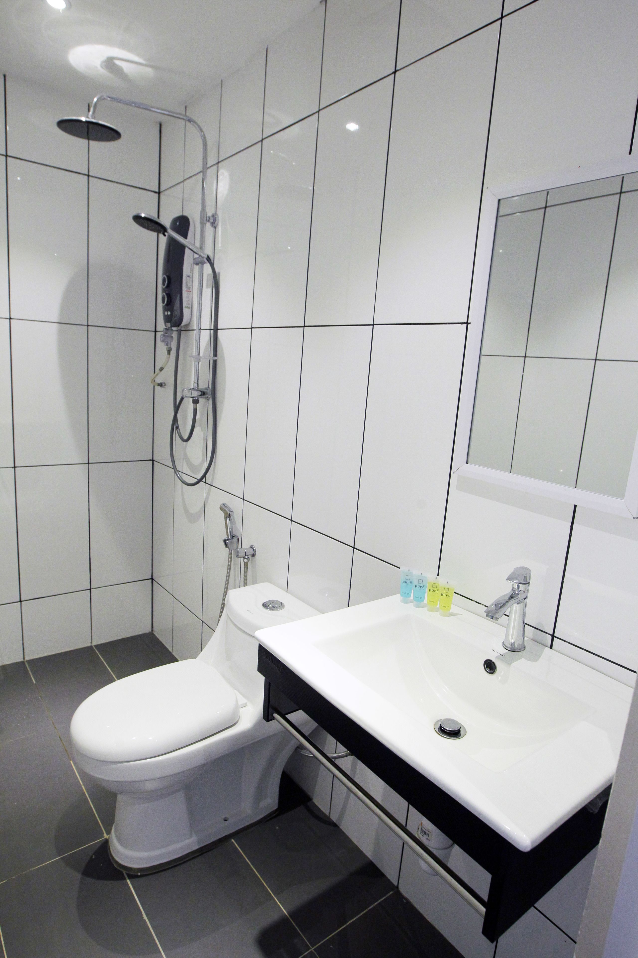 Une salle de bain moderne avec des toilettes blanches, un lavabo blanc et une douche équipée d’un pommeau de douche à main.