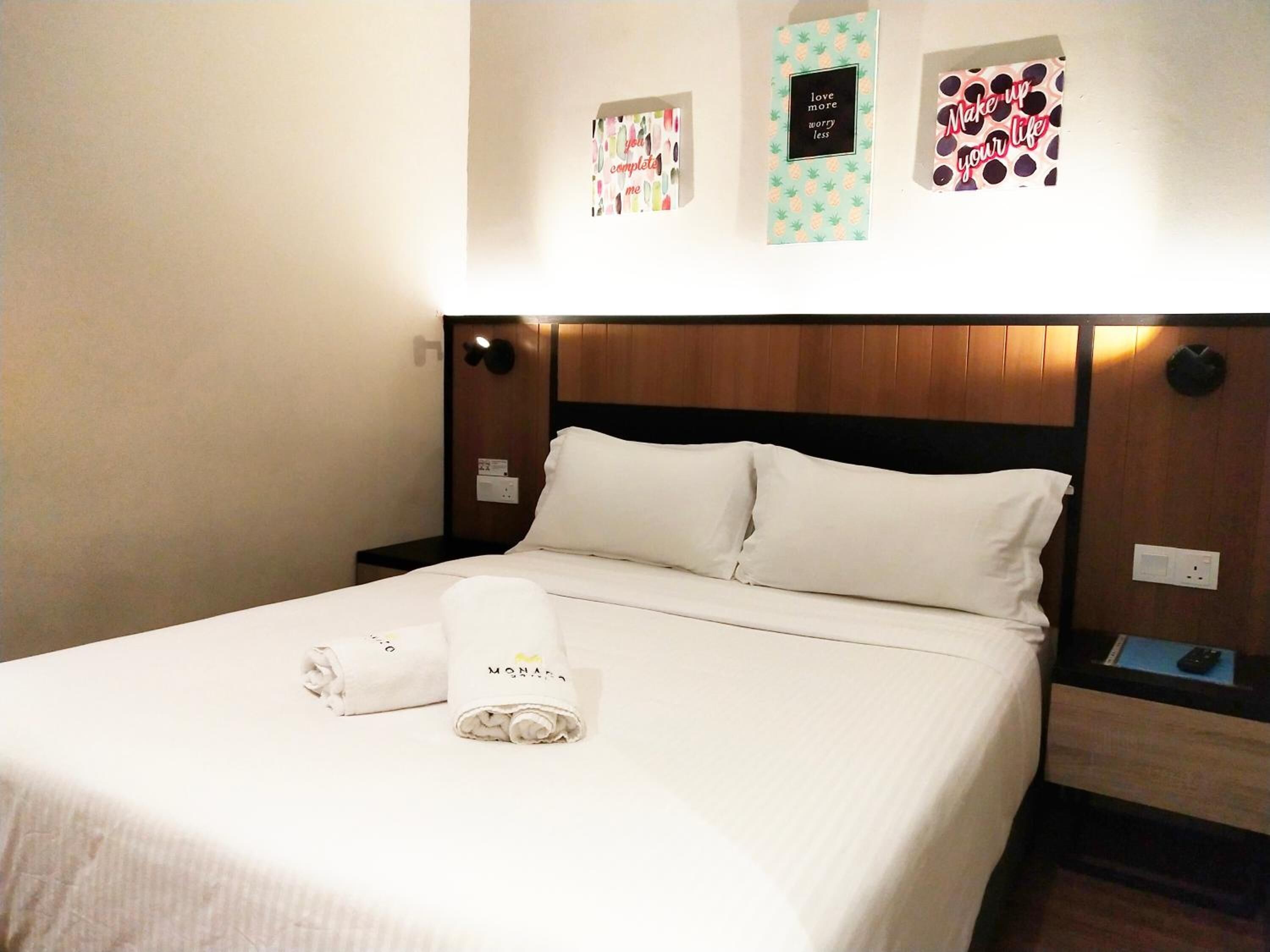 A hotel room with a neatly made bed, a nightstand with a remote control, and wall decorations including a framed quote and a framed picture.
