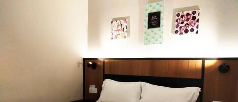 A hotel room with a neatly made bed, a nightstand with a remote control, and wall decorations including a framed quote and a framed picture.