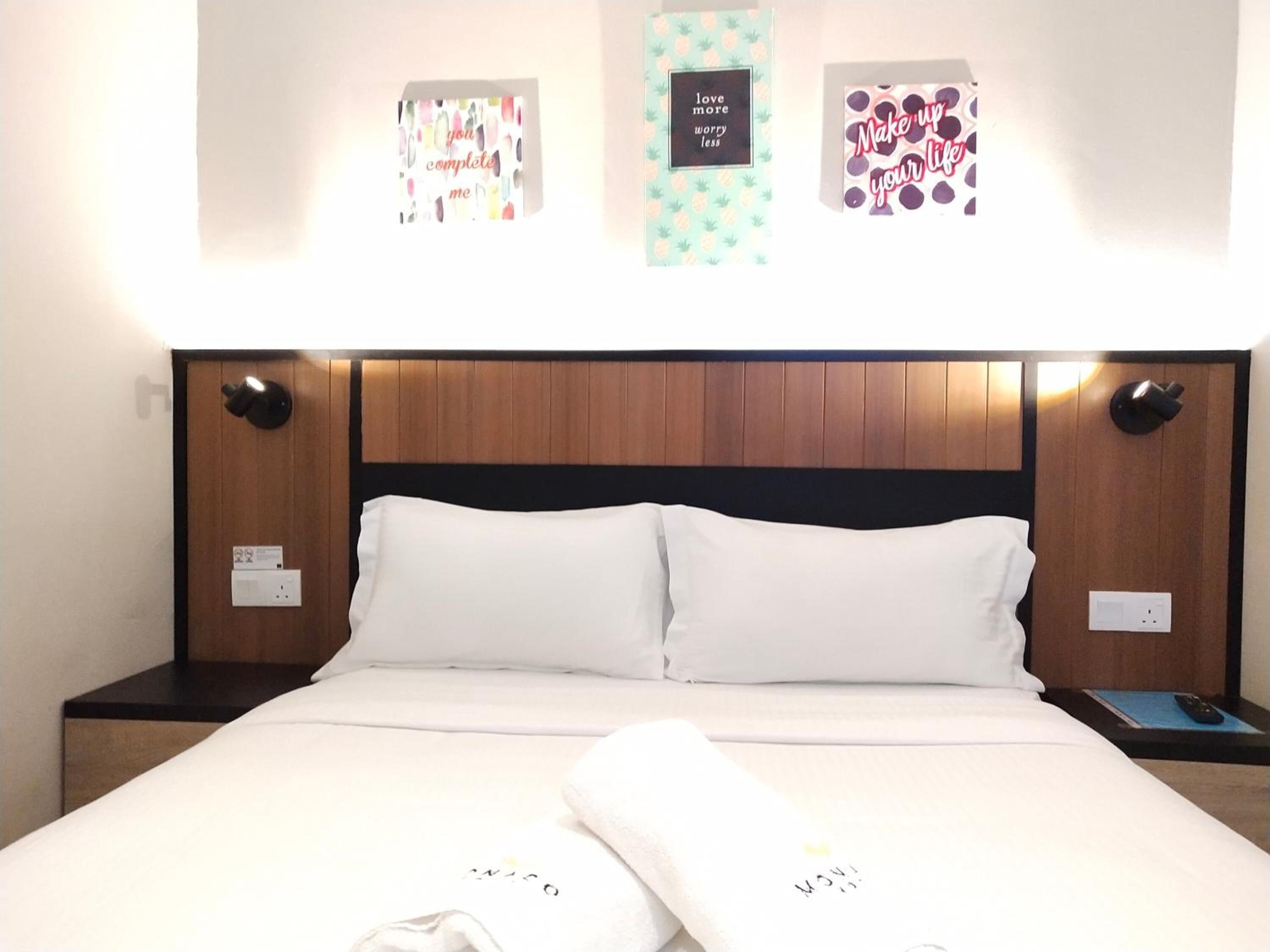 Habitación de hotel con cabecera de madera, ropa de cama blanca y tres adornos de pared con citas motivacionales.