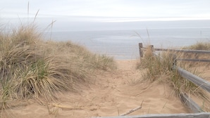 A sandy beach path leading to the sea, surrounded by grass and wooden barriers.