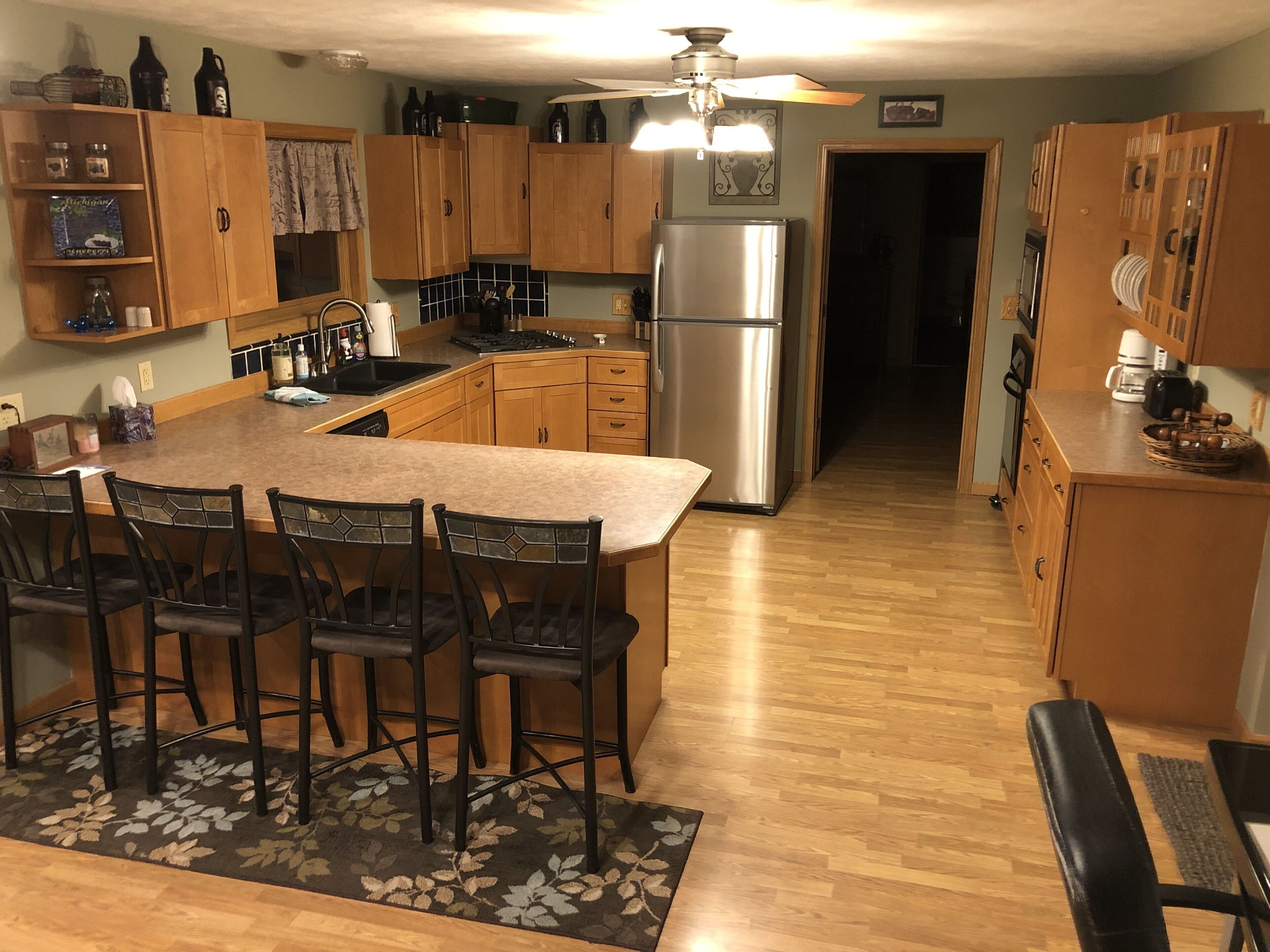 A kitchen with wooden cabinets, a stainless steel refrigerator, a dining area with chairs, and a central island.