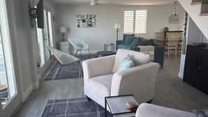 Un salón moderno con un sofá blanco, una mesita auxiliar y una zona de comedor con una mesa y sillas de madera.