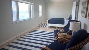 Un dormitorio con cama, dos ventanas, alfombra a rayas y sillas de mimbre.