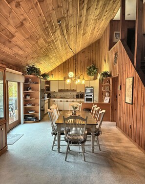 A wooden interior with a dining table and chairs, a kitchen area, and a staircase.