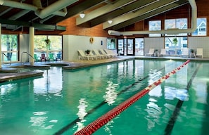 Ein Hallenbad mit deutlich abgetrennten Bahnen, Liegestühlen und Blick ins Freie.