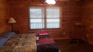 Habitación de cabaña de madera con cama, una silla, ventana con persianas y ventilador de techo.