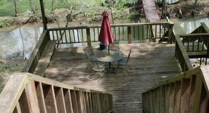 A wooden deck with a round table and chairs, a red umbrella, and a wooden railing.