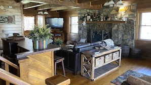 Een rustiek interieur van een blokhut met een stenen open haard, houten meubels en een televisie.
