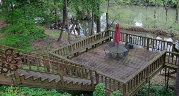 A wooden deck with a table and chairs, surrounded by trees and a body of water.