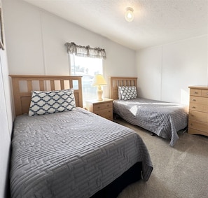 A bedroom with two beds, a nightstand with a lamp, a dresser, and a window with a curtain. - 3 Bedroom Palm Key Village Home - PK015 (Davenport)