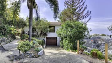 Situated in a lush environment, this two-story house features a prominent front entrance and a paved driveway leading to a small garden.