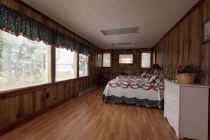 Un dormitorio con paneles de madera, una chimenea de piedra, una cama con colcha, un aparador y una ventana con persianas.