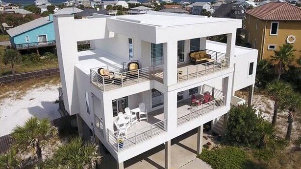 Una moderna casa a più piani con un balcone, un patio con mobili da esterno e vista sull'oceano.