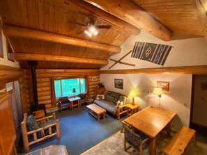 A cozy log cabin interior with a wooden ceiling, a sofa, a table, and a bench. - Sleeping Wolf Cabin: 2BR w/ ski trail & river access, pool/hot tub, laundry (Winthrop)