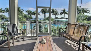 A balcony with two chairs, a small table, and a view of a pool and palm trees. - 406 Mariners Club - 3 bedroom elegant tri-level townhome with views of the ocean (Tavernier)