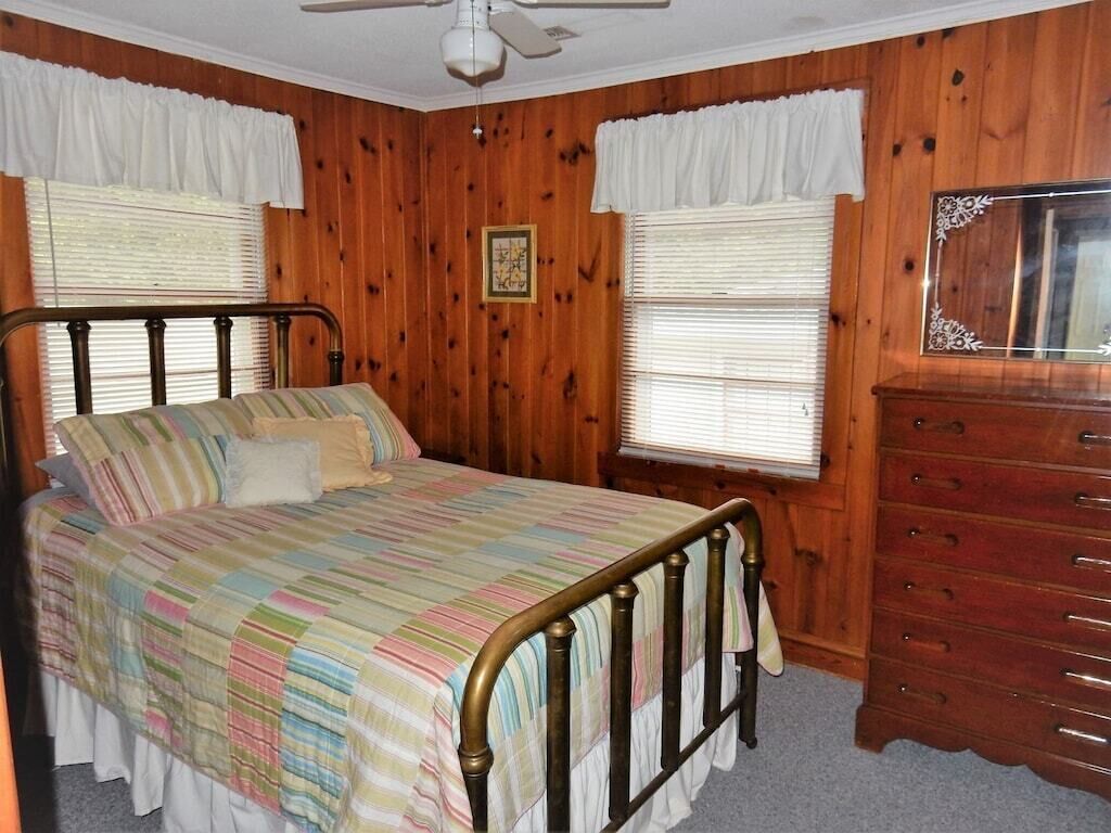 Un dormitorio con cama, paredes de madera, cómoda y ventilador de techo.